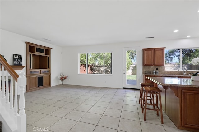 kitchen featuring sink, a breakfast bar, backsplash, dark stone counters, and light tile patterned floors