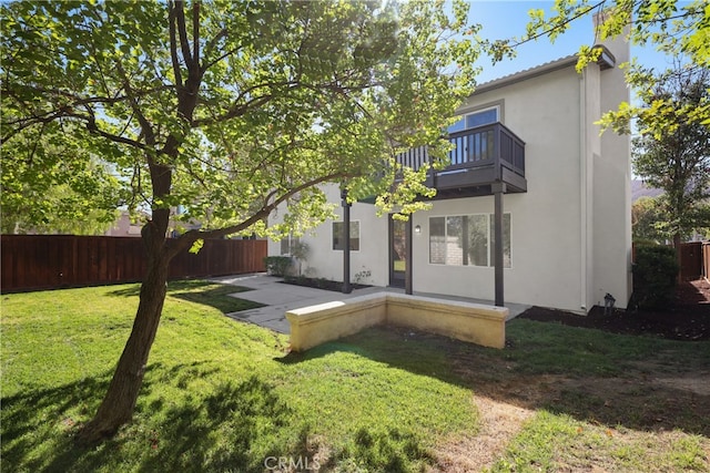 rear view of house with a balcony, a patio, and a lawn