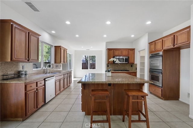 kitchen featuring decorative backsplash, stainless steel appliances, sink, a center island, and light stone counters