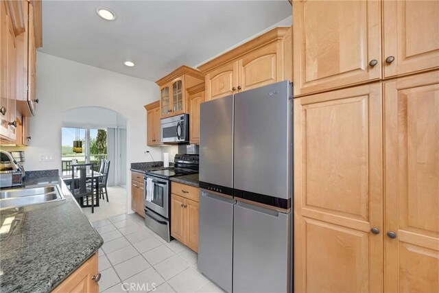 kitchen featuring dark stone counters, stainless steel appliances, sink, light brown cabinets, and light tile patterned flooring