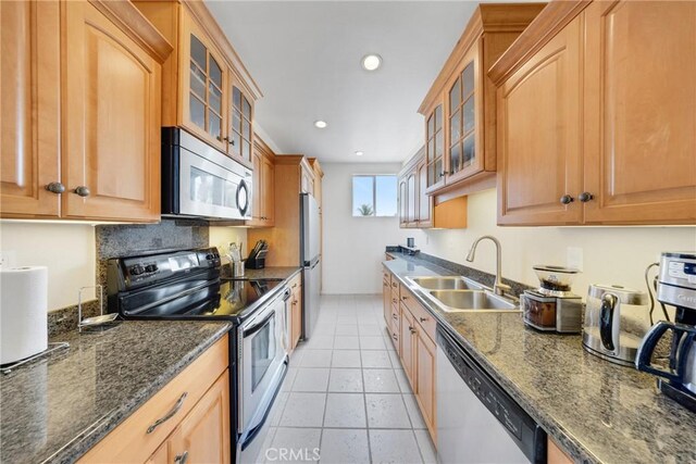 kitchen featuring appliances with stainless steel finishes, light tile patterned floors, dark stone counters, and sink