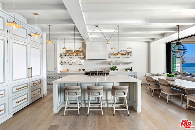 kitchen with an island with sink, light hardwood / wood-style floors, hanging light fixtures, beam ceiling, and a kitchen bar