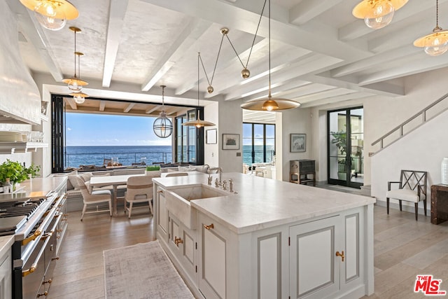 kitchen featuring a water view, light wood-type flooring, a kitchen island with sink, white cabinets, and hanging light fixtures