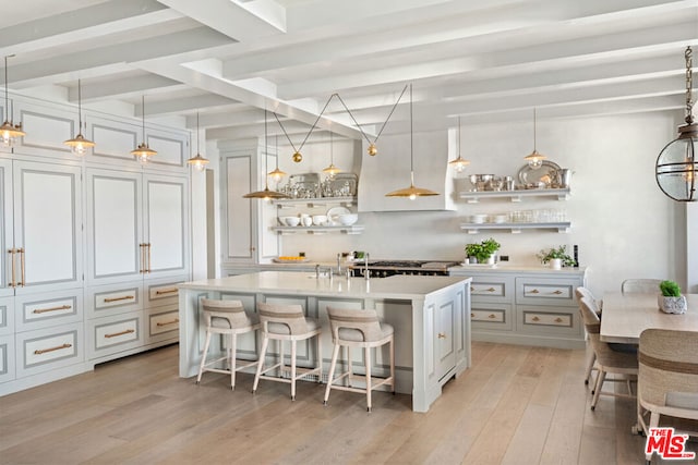 kitchen with beamed ceiling, hanging light fixtures, a center island with sink, light hardwood / wood-style flooring, and a kitchen breakfast bar