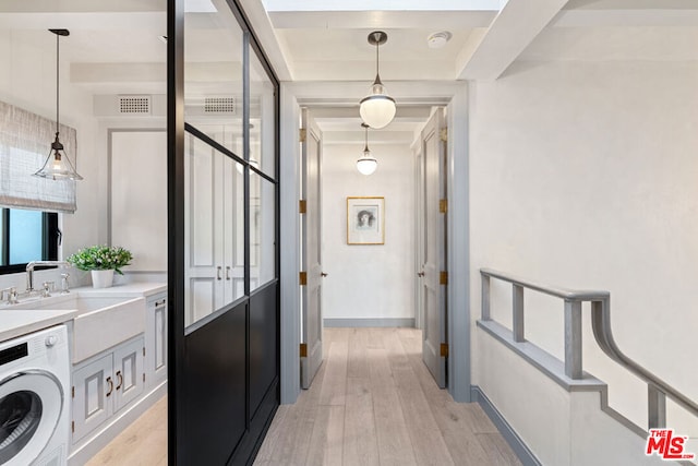 hallway with light wood-type flooring, sink, and washer / dryer