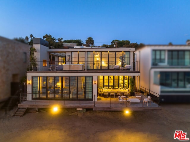 back house at dusk featuring a balcony, an outdoor living space, and a patio