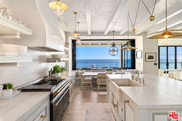 kitchen with light stone counters, white cabinets, dark wood-type flooring, high end stove, and a water view