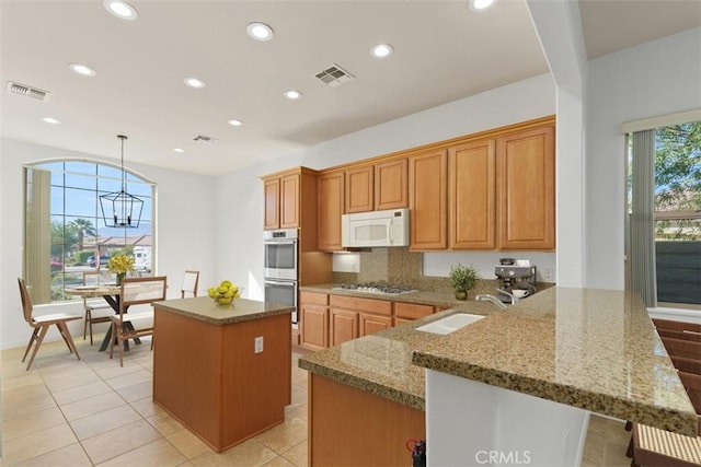 kitchen featuring kitchen peninsula, stainless steel appliances, decorative light fixtures, a kitchen island, and sink