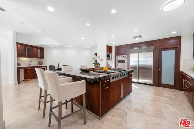 kitchen featuring built in appliances, a breakfast bar, a kitchen island, and dark stone counters