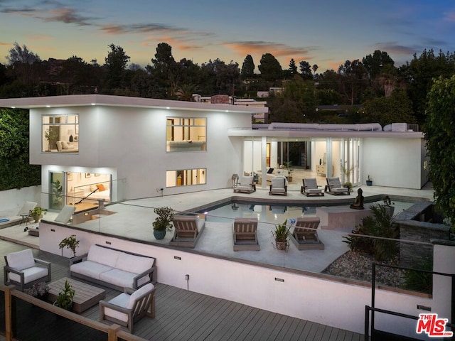 back house at dusk with outdoor lounge area and a swimming pool side deck