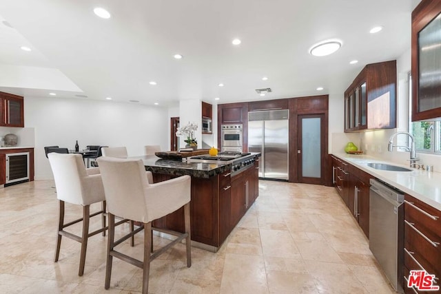 kitchen with a kitchen breakfast bar, beverage cooler, sink, built in appliances, and a center island