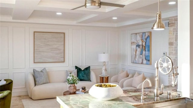 living room featuring ceiling fan, coffered ceiling, and sink