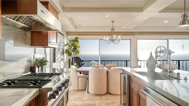 kitchen featuring stainless steel appliances, beverage cooler, wall chimney range hood, a water view, and hanging light fixtures