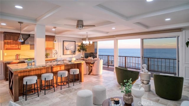 interior space featuring coffered ceiling, ceiling fan with notable chandelier, a water view, a beach view, and beamed ceiling