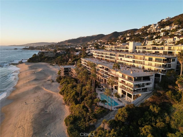 aerial view at dusk featuring a water view and a view of the beach