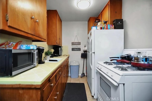 kitchen featuring tile countertops, white gas range, sink, and light tile patterned floors