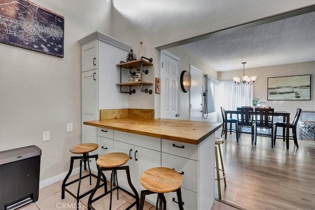 kitchen with a kitchen breakfast bar, butcher block counters, white cabinets, and pendant lighting