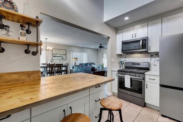 kitchen featuring wooden counters, appliances with stainless steel finishes, white cabinetry, and hanging light fixtures