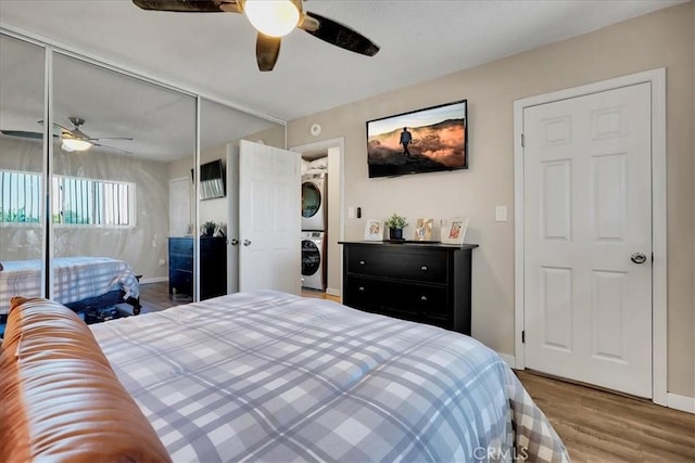 bedroom with hardwood / wood-style flooring, ceiling fan, stacked washer / dryer, and a closet