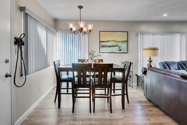 dining area featuring a textured ceiling, light hardwood / wood-style flooring, and an inviting chandelier