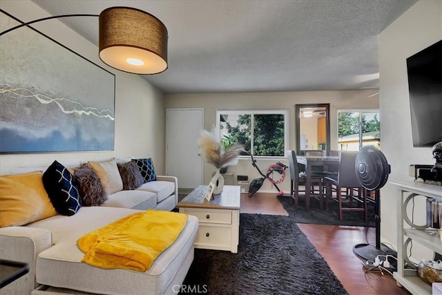 living room with a textured ceiling, ceiling fan, and dark wood-type flooring