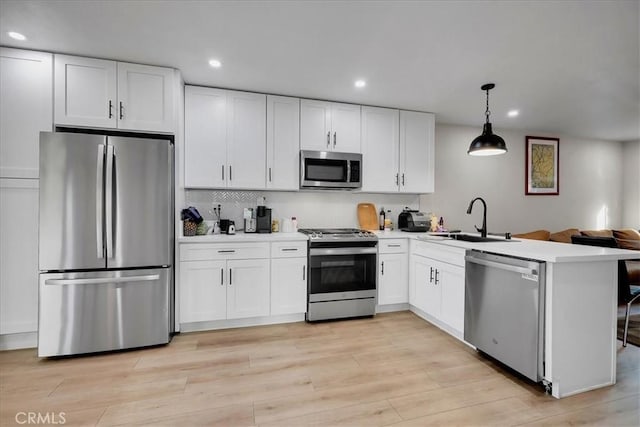 kitchen with kitchen peninsula, appliances with stainless steel finishes, decorative light fixtures, and white cabinetry