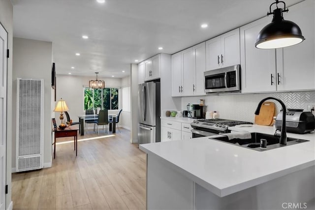 kitchen with sink, light hardwood / wood-style floors, decorative light fixtures, white cabinets, and appliances with stainless steel finishes