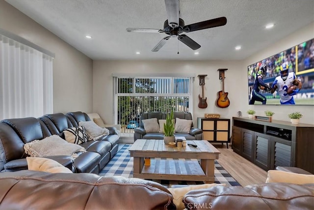 living room with ceiling fan, light wood-type flooring, and a textured ceiling