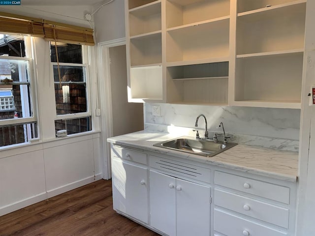 kitchen with decorative backsplash, light stone counters, dark wood-type flooring, sink, and white cabinetry