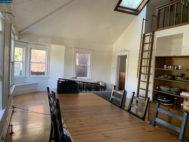 dining room with beam ceiling, a skylight, light hardwood / wood-style flooring, and high vaulted ceiling