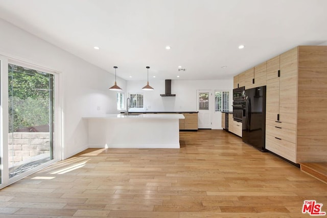 kitchen featuring wall chimney exhaust hood, hanging light fixtures, black fridge, kitchen peninsula, and light hardwood / wood-style flooring