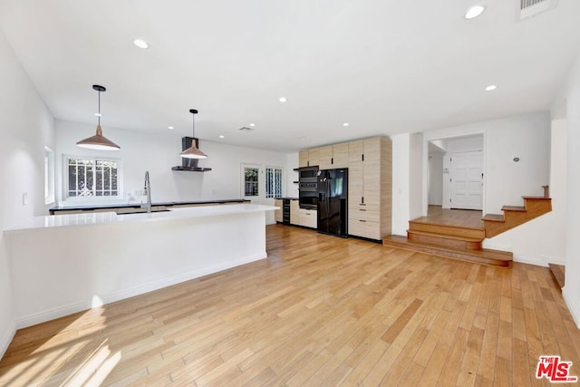 kitchen featuring wall chimney exhaust hood, decorative light fixtures, sink, black fridge, and light hardwood / wood-style flooring