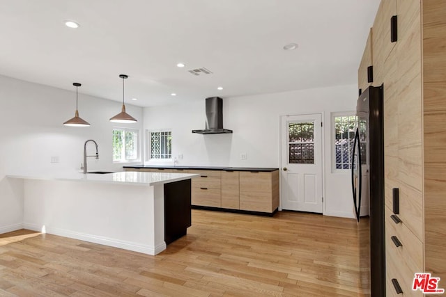 kitchen with decorative light fixtures, light hardwood / wood-style floors, light brown cabinets, and wall chimney exhaust hood