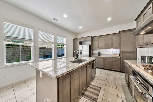 kitchen featuring sink, stainless steel appliances, light stone counters, a center island with sink, and light tile patterned floors