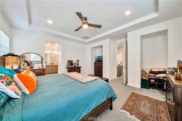 bedroom featuring ensuite bathroom, ceiling fan, light colored carpet, and a tray ceiling