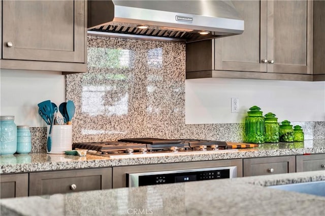 kitchen featuring wall chimney range hood, wall oven, light stone counters, backsplash, and stainless steel gas stovetop