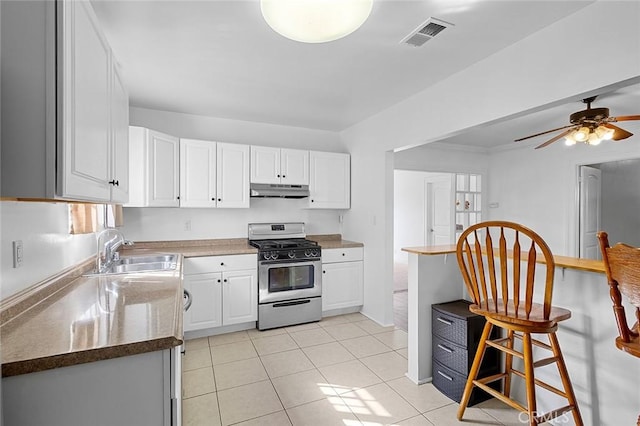 kitchen with stainless steel gas range oven, sink, light tile patterned floors, and white cabinets