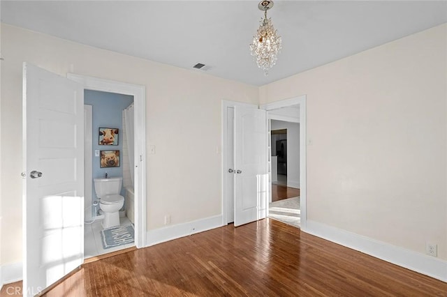 unfurnished bedroom with ensuite bath, hardwood / wood-style floors, and a notable chandelier