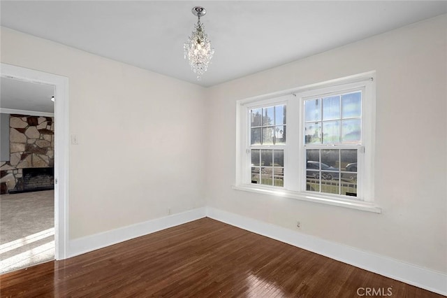 unfurnished room with an inviting chandelier, a stone fireplace, and wood-type flooring