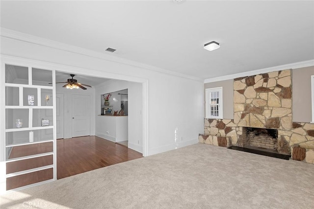 unfurnished living room featuring crown molding, a stone fireplace, carpet flooring, and ceiling fan