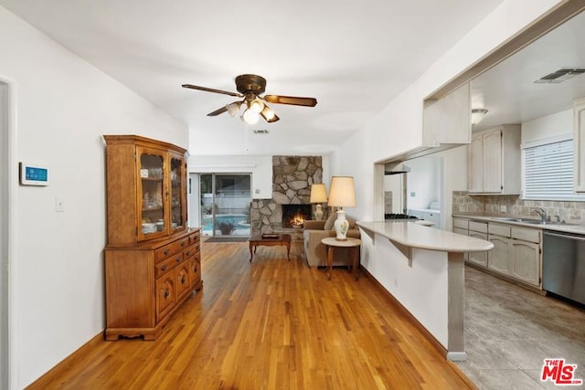 kitchen with tasteful backsplash, a stone fireplace, stainless steel dishwasher, kitchen peninsula, and light wood-type flooring