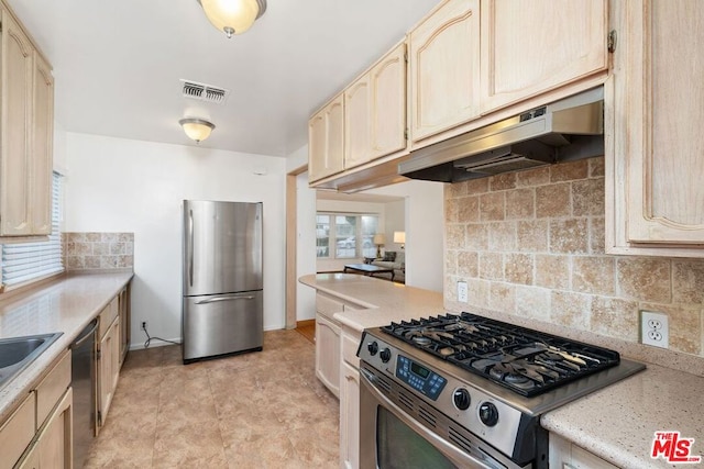 kitchen with light brown cabinetry, backsplash, and stainless steel appliances