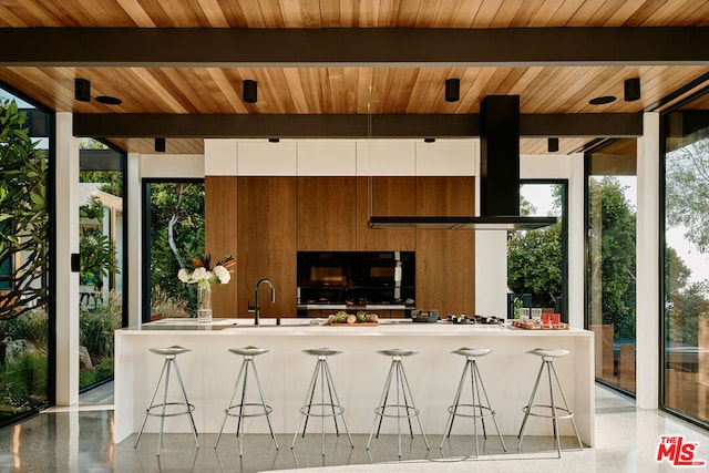 kitchen featuring beamed ceiling, wood ceiling, extractor fan, white cabinetry, and a wall of windows