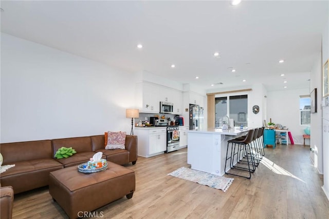 kitchen with a kitchen island with sink, white cabinets, light wood-type flooring, appliances with stainless steel finishes, and a breakfast bar area