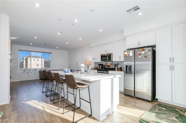 kitchen featuring white cabinetry, an island with sink, a breakfast bar area, appliances with stainless steel finishes, and light wood-type flooring