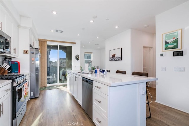 kitchen with a breakfast bar, a kitchen island with sink, white cabinets, sink, and appliances with stainless steel finishes