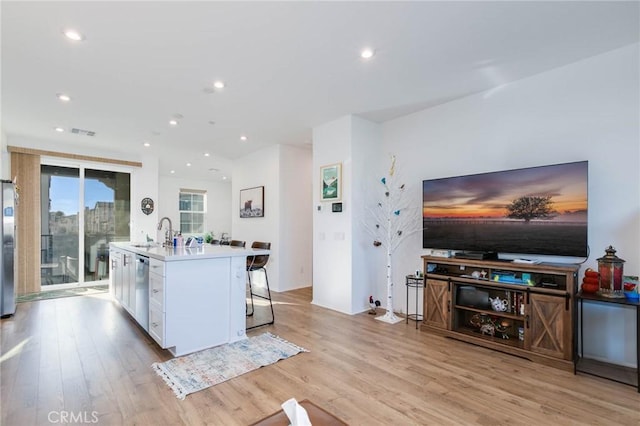 kitchen featuring stainless steel appliances, a kitchen breakfast bar, an island with sink, light hardwood / wood-style floors, and white cabinets