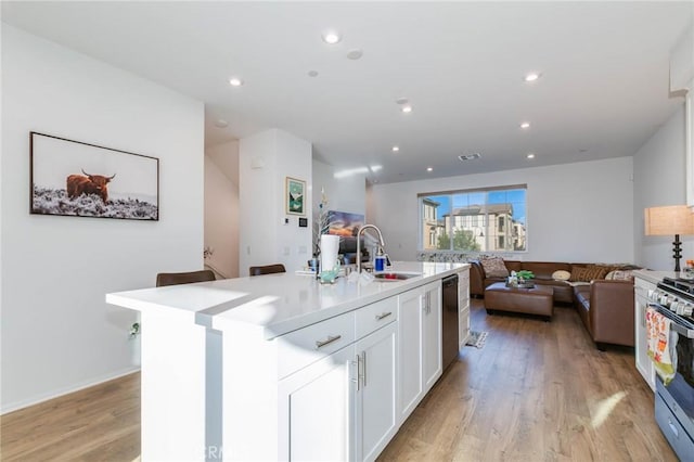 kitchen with white cabinetry, sink, light wood-type flooring, a kitchen island with sink, and appliances with stainless steel finishes