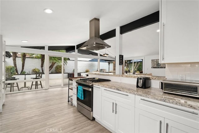 kitchen featuring wall chimney exhaust hood, light stone countertops, white cabinetry, and stainless steel range with gas stovetop