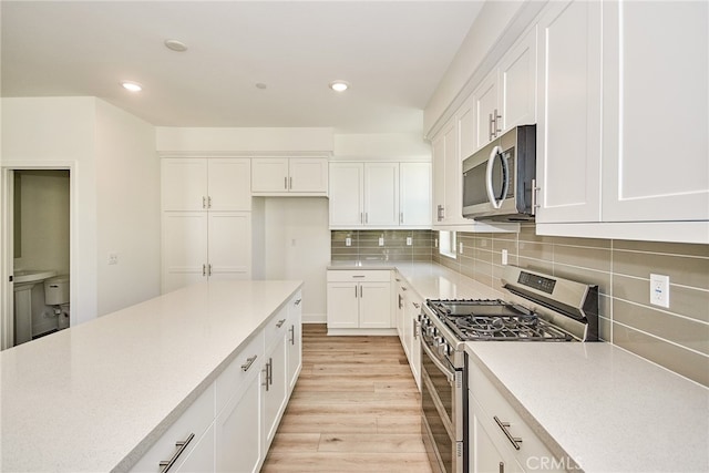 kitchen featuring appliances with stainless steel finishes, decorative backsplash, white cabinetry, and light hardwood / wood-style flooring